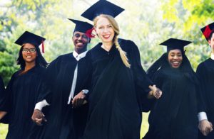 Happy And Young Smiling Graduates In Their Academic Dress.