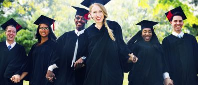 Happy And Young Smiling Graduates In Their Academic Dress.