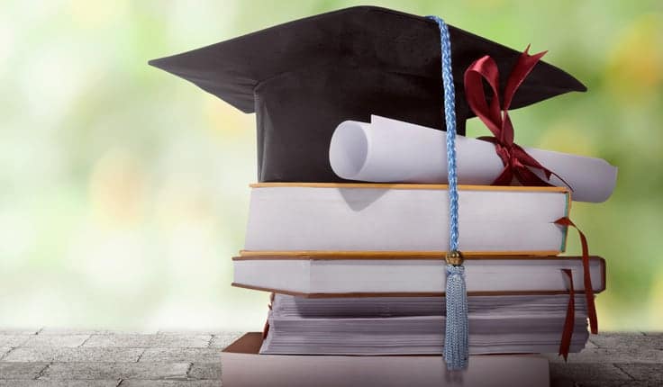 A Table With Graduate Cap Placed Over The Bunch of Books.