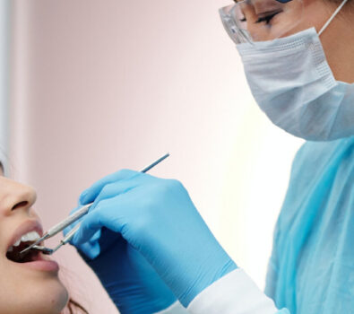 A female dentist with specs oh ger eyes , head , nose , mouth and hand covered with masks and gloves performing a dental examination for a young femal patient.