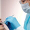 A female dentist with specs oh ger eyes , head , nose , mouth and hand covered with masks and gloves performing a dental examination for a young femal patient.