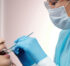 A female dentist with specs oh ger eyes , head , nose , mouth and hand covered with masks and gloves performing a dental examination for a young femal patient.