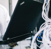A field engineer is standing at the electrical wiring room with a laptop on his hand.
