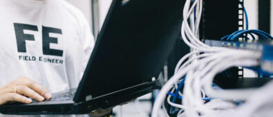 A field engineer is standing at the electrical wiring room with a laptop on his hand.