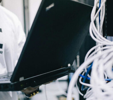 A field engineer is standing at the electrical wiring room with a laptop on his hand.