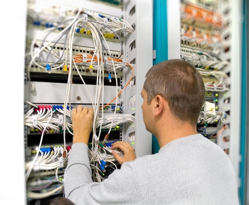 A man is fixing electrical wiring at the electrical wiring panel.